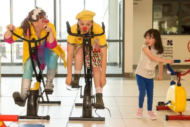 Two Clowndoctors on stationary exercise bikes in hospital
